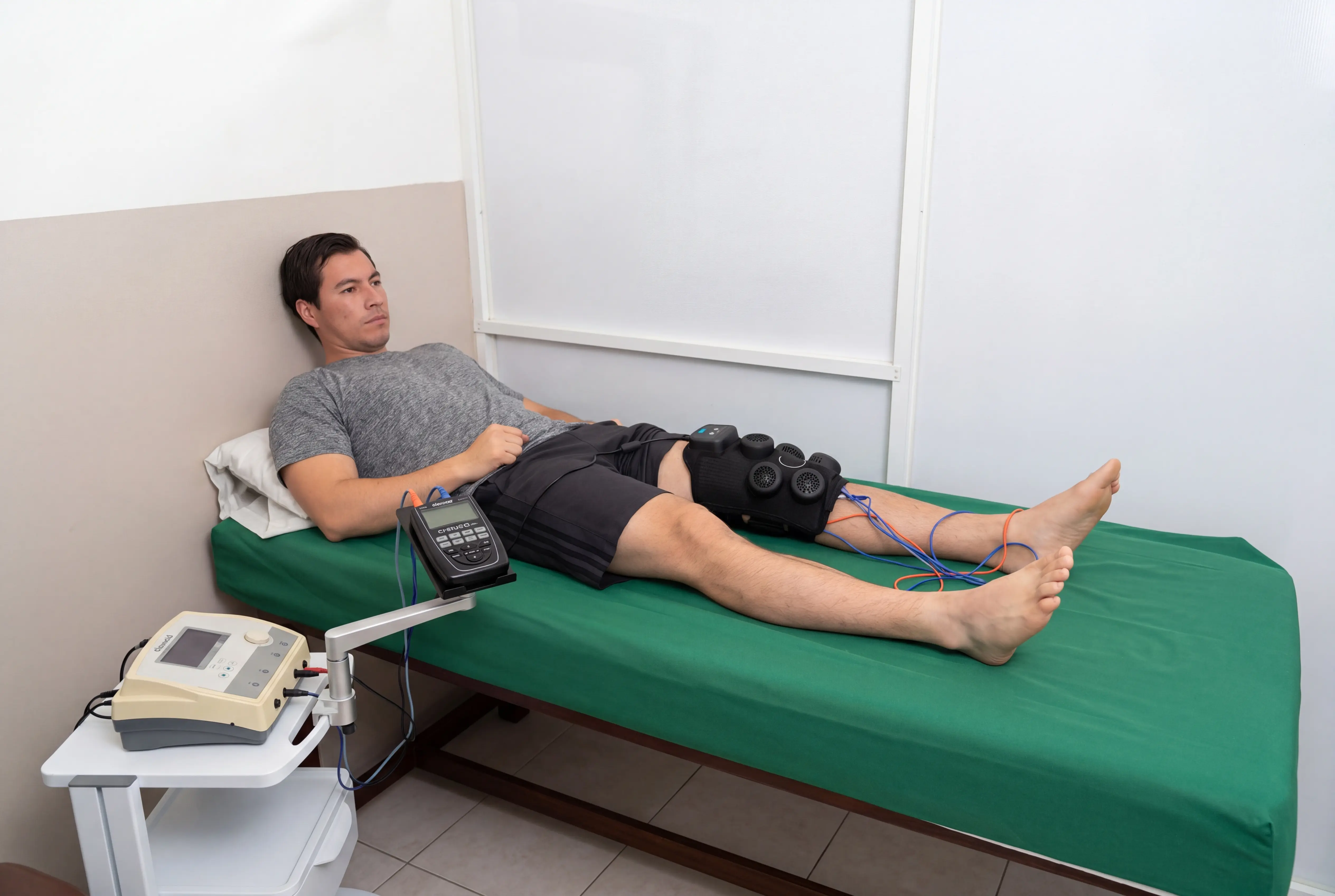 Electroestimulación en rodilla con manguito y electrodos durante sesión de fisioterapia.