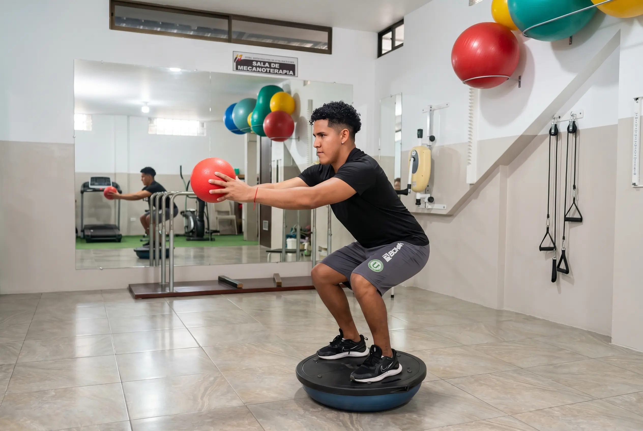 Sesión de mecanoterapia: ejercicio funcional sobre plataforma inestable con balón medicinal.